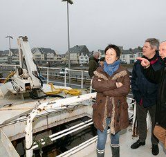 1 femme et 2 hommes sur le pont d'un bateau de pêche à quai